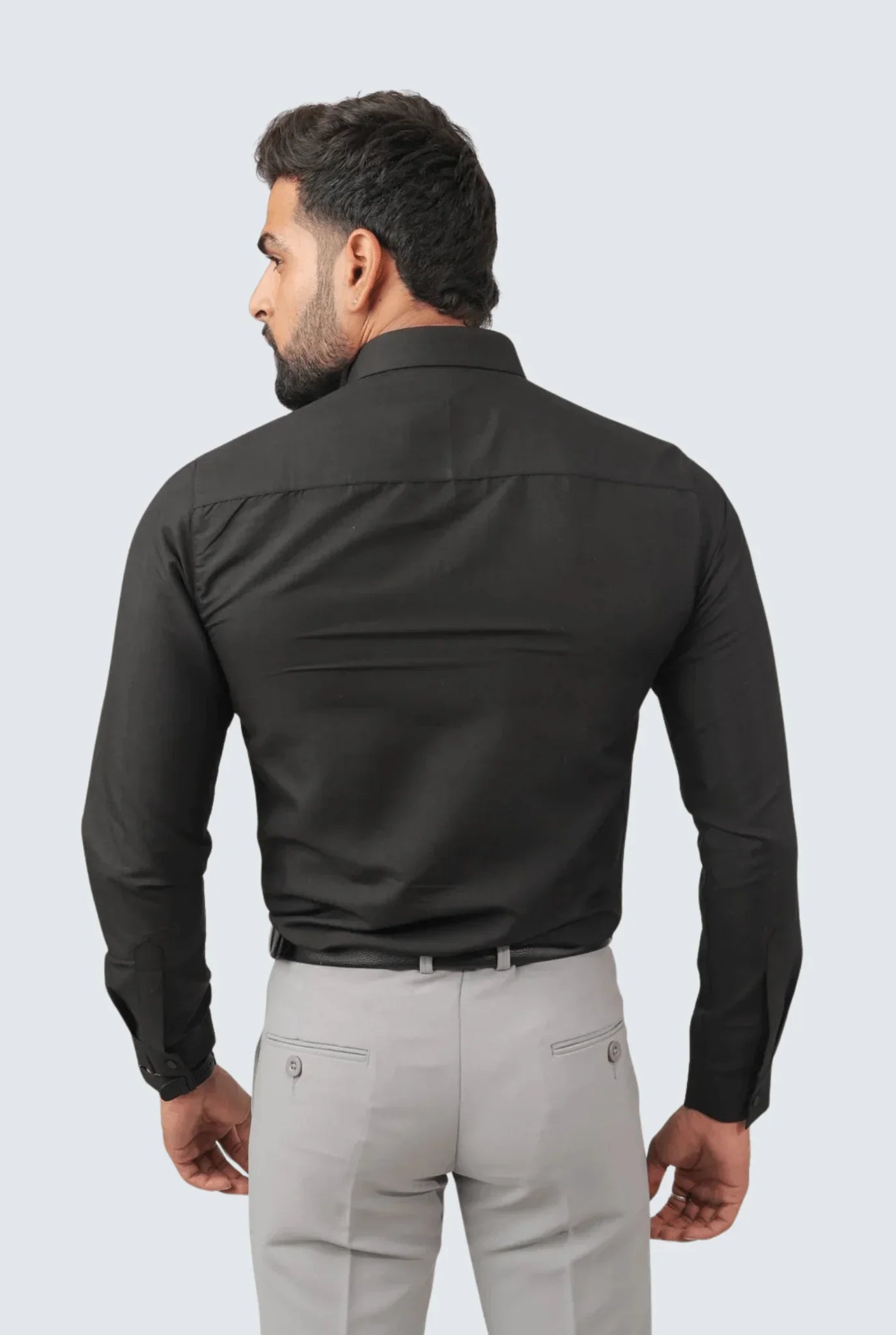 Man wearing black slim fit cotton shirt and light gray trousers, viewed from back