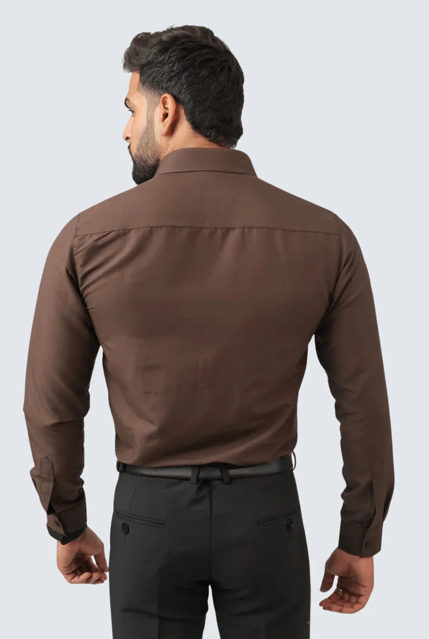 Rear view of man wearing slim fit brown cotton shirt and black trousers against light background