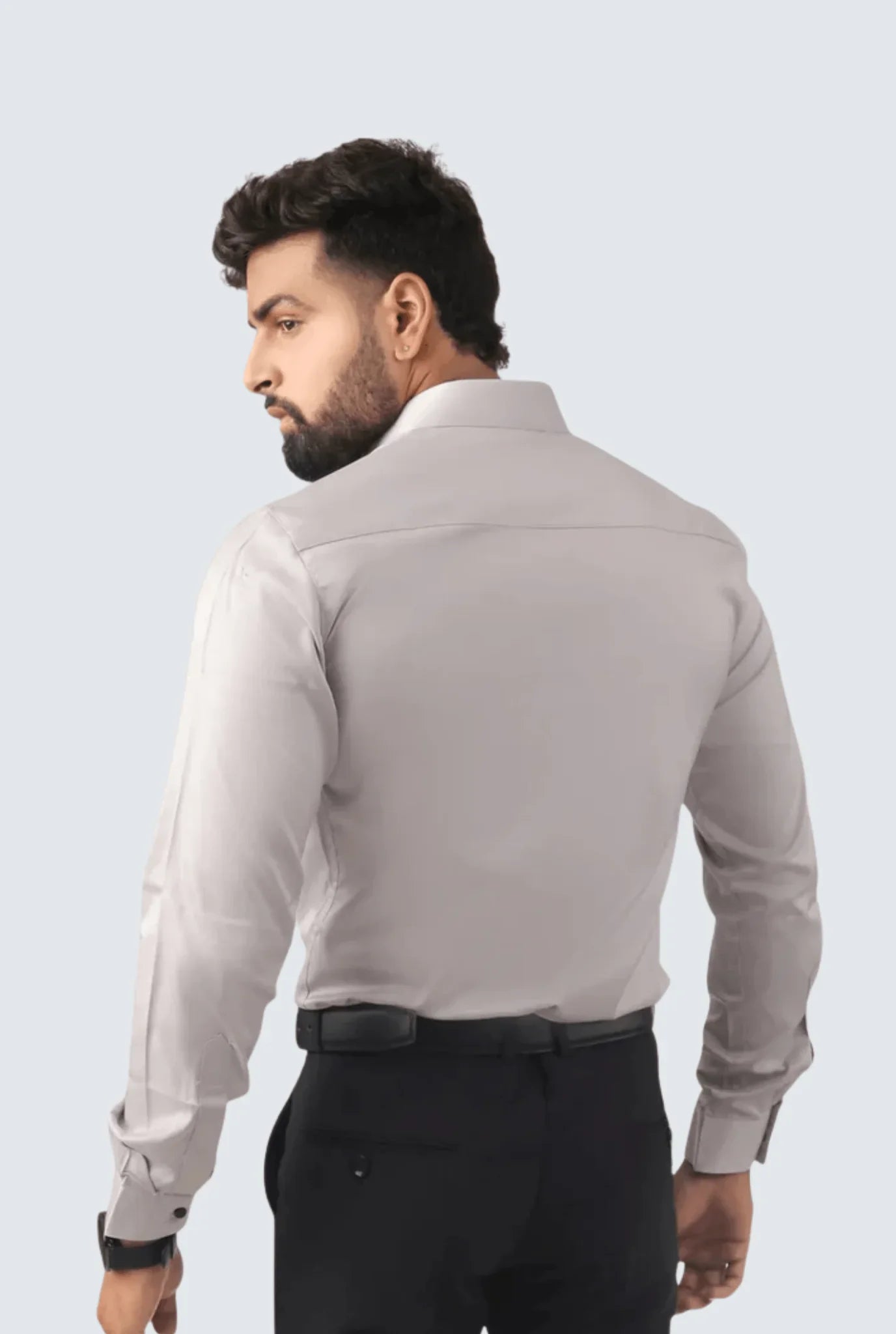 Man wearing gray satin shirt and black pants, posing with back turned against plain background