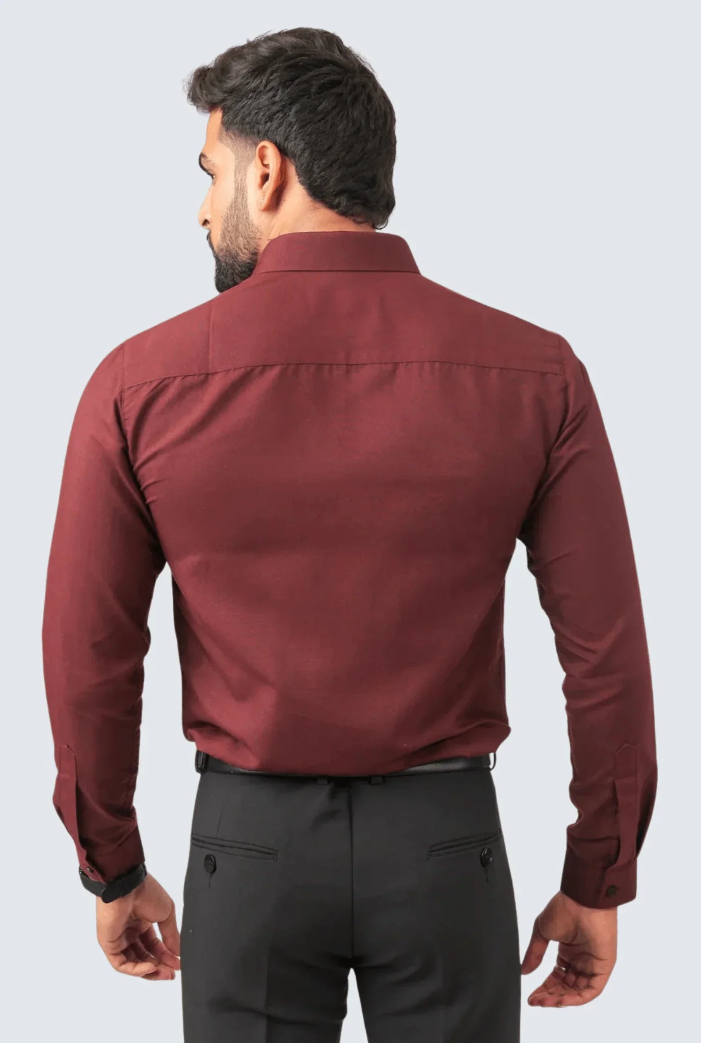 Back view of man wearing maroon cotton slim fit formal shirt with black trousers against light background
