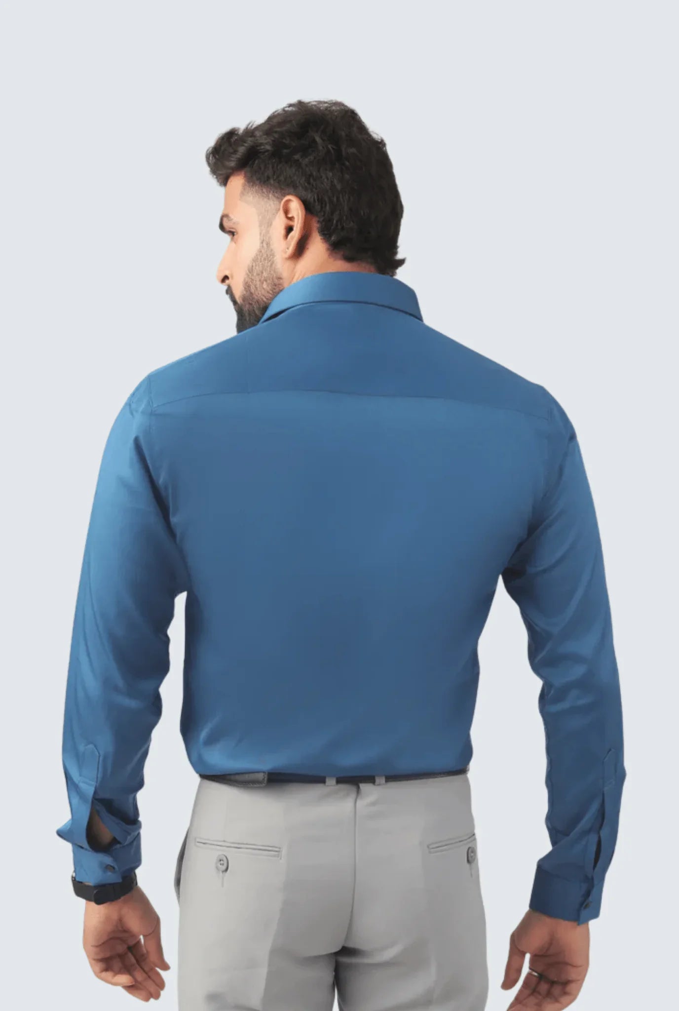 Man wearing a blue satin smart fit premium shirt paired with light grey trousers, back view