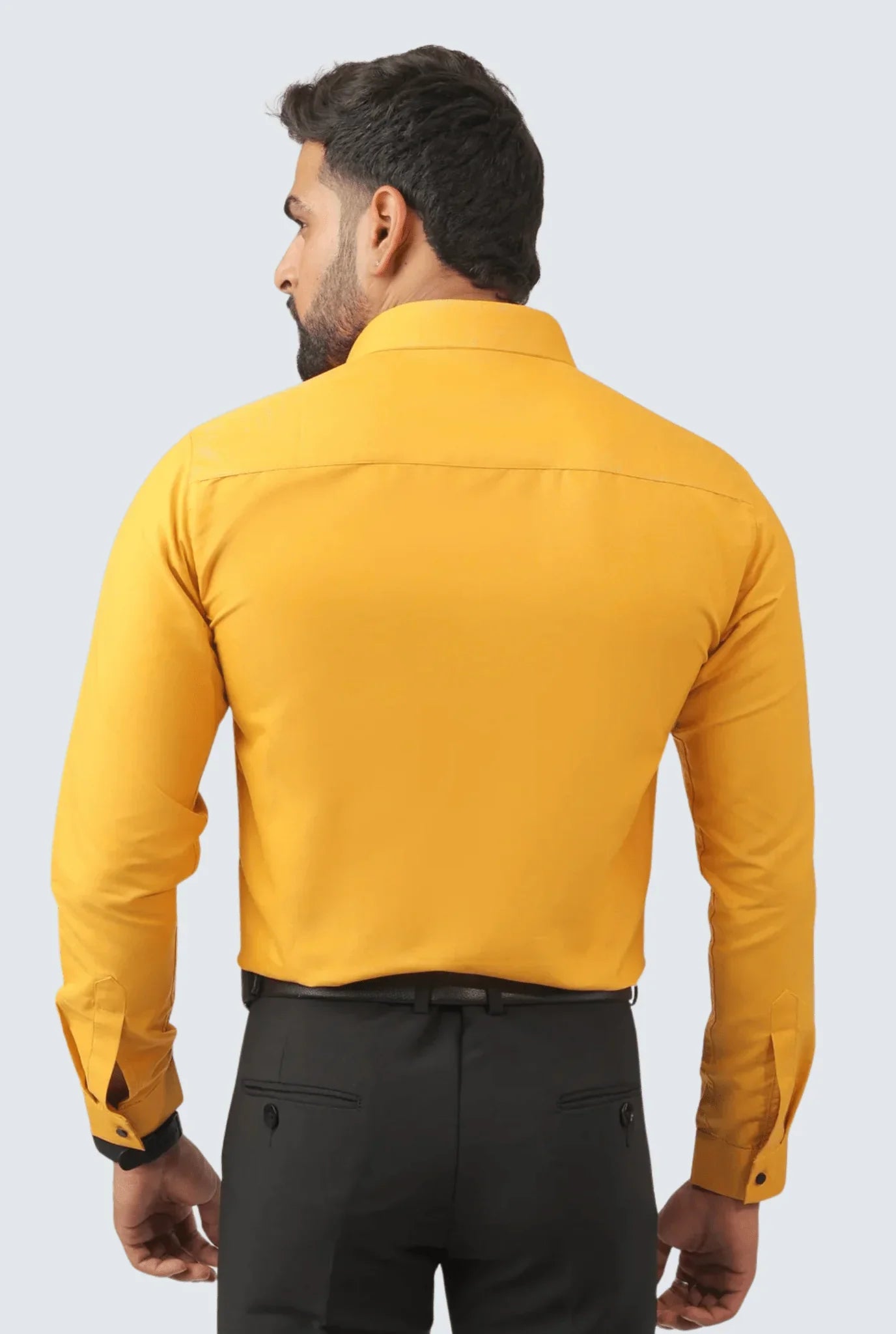 Back view of man wearing mustard yellow cotton formal shirt with black trousers on gray background
