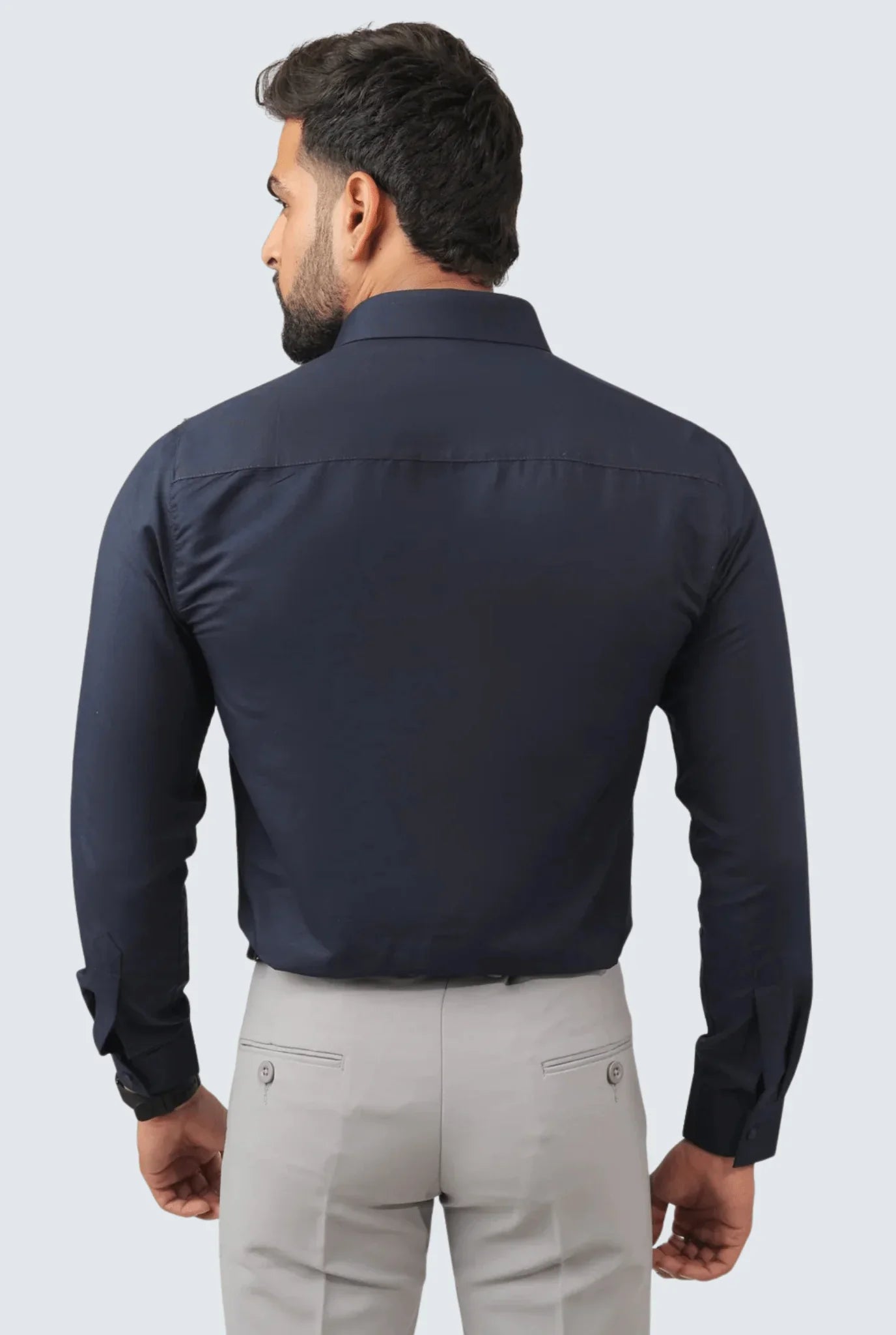 Back view of man wearing navy blue slim fit cotton shirt with light gray pants