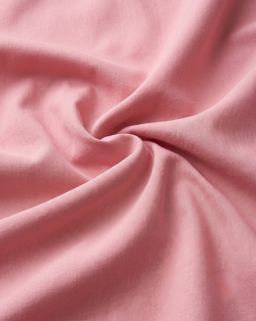 Pink cotton shirt fabric close-up with soft drape and wrinkles
