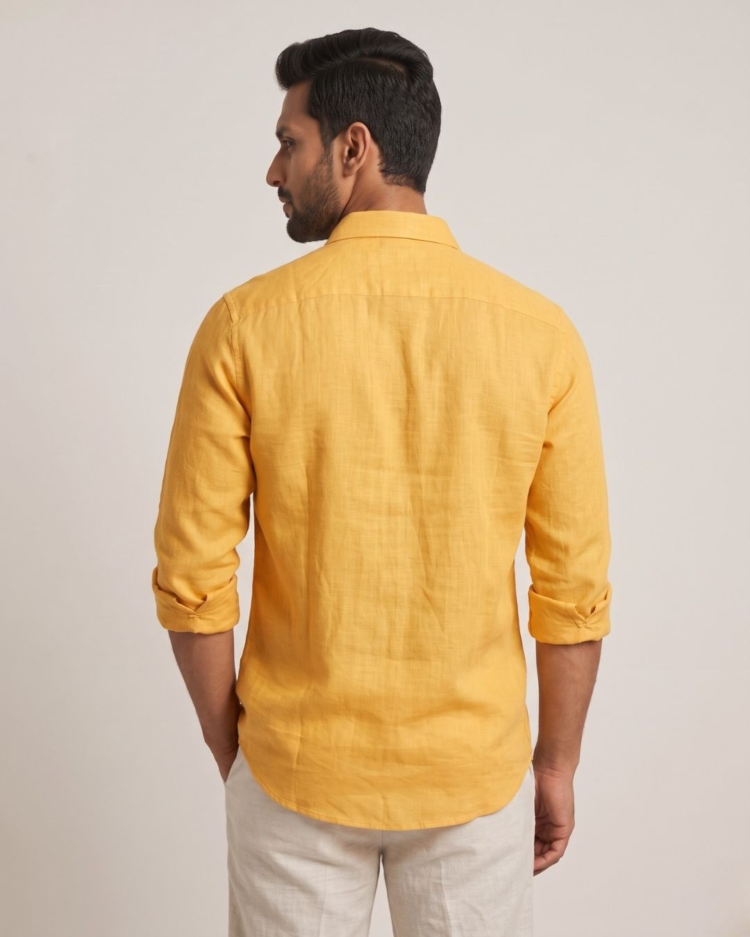 Back view of a yellow linen shirt with rolled sleeves and a curved hem