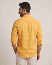 Back view of a yellow linen shirt with rolled sleeves and a curved hem